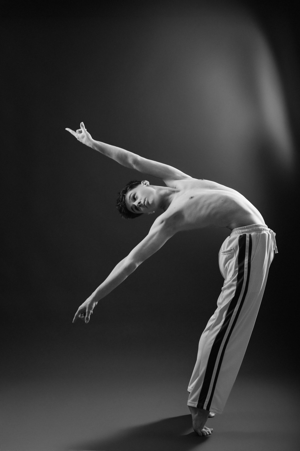 A male dancer's bare feet and outstretched hand caught mid-movement in dramatic side lighting, from a Delight Images dance session